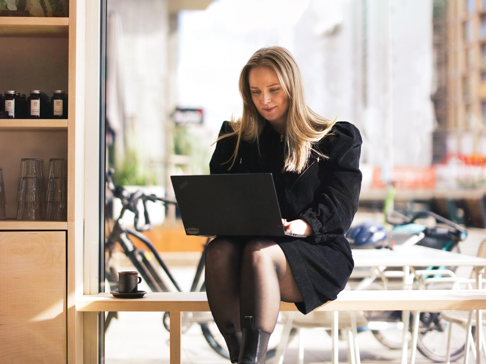 Stine Martine Lefdal sitter på en benk på en café og jobber på dataen